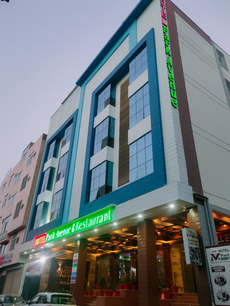 Hotel Park Avenue Sikar full building facade at dusk with glowing neon sign and blue glass panels